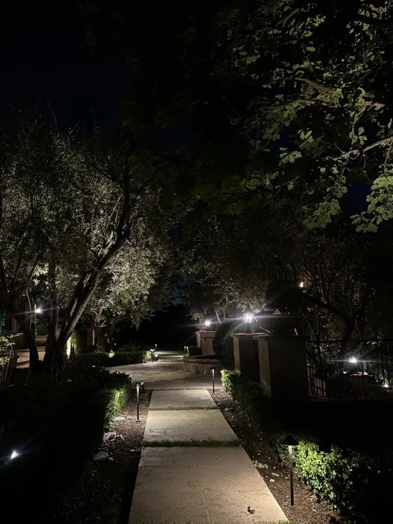Long driveway pathway lighting with tree uplighting and gate lanterns at night