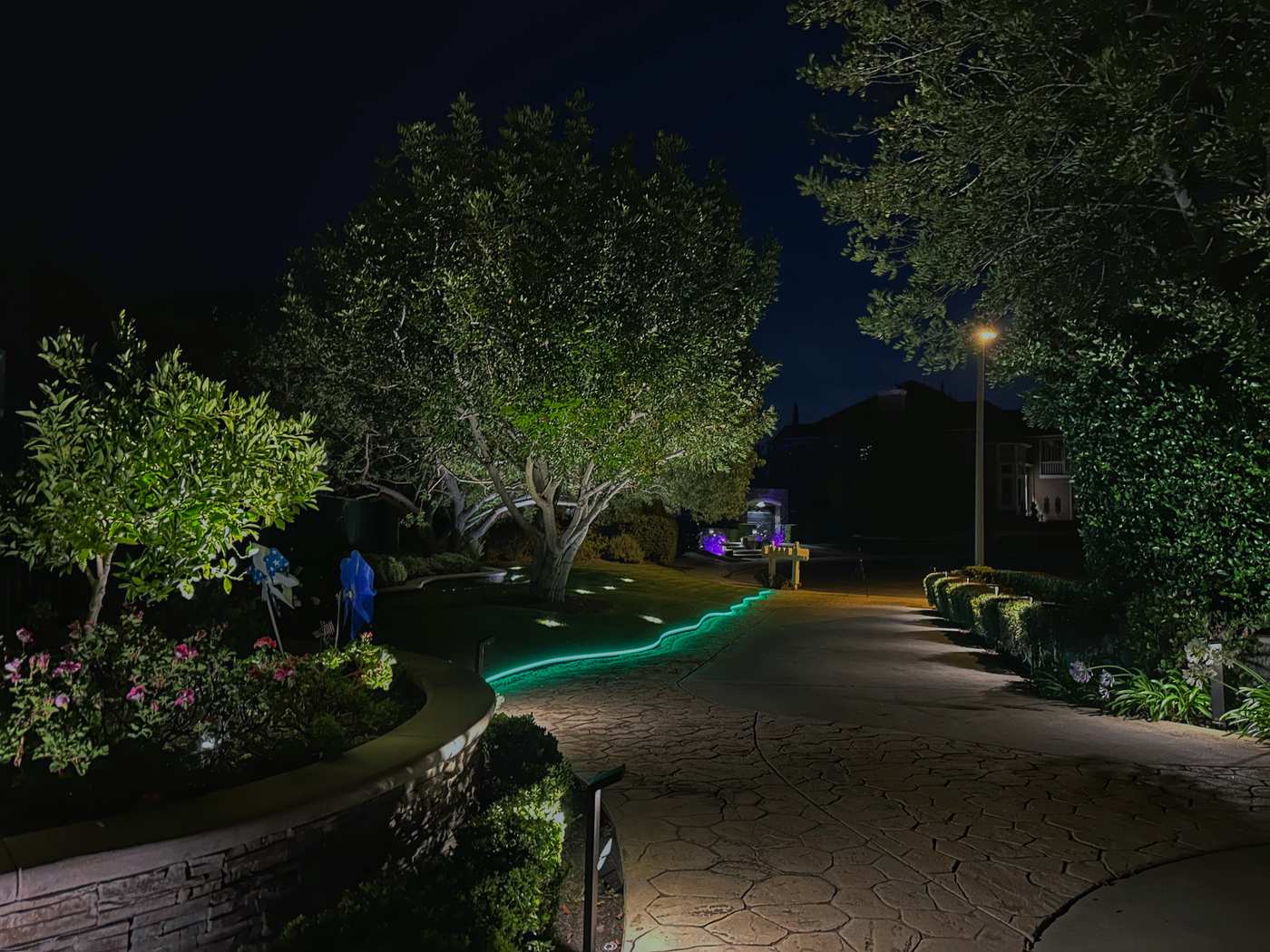 Stamped concrete driveway edge in Coto de Caza, CA outlined with a green color-changing LED strip light winding along the stonework toward the front entry at night.